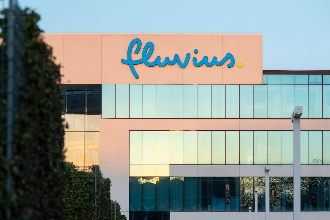 Le logo Fluvius sur la façade d'un immeuble de bureaux, avec du lierre et un lampadaire au premier plan au coucher du soleil