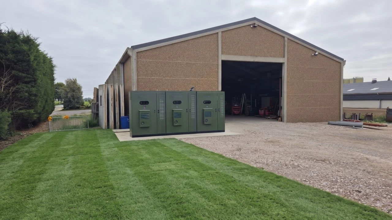 Drei grüne Batterie- und Wechselrichterschränke mit Fernsteuerungseinheit neben einer Industriehalle